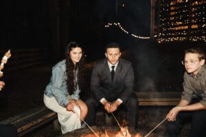 Couple sitting on wooden benches around a firepit roasting marshmallows at All4One Farms.